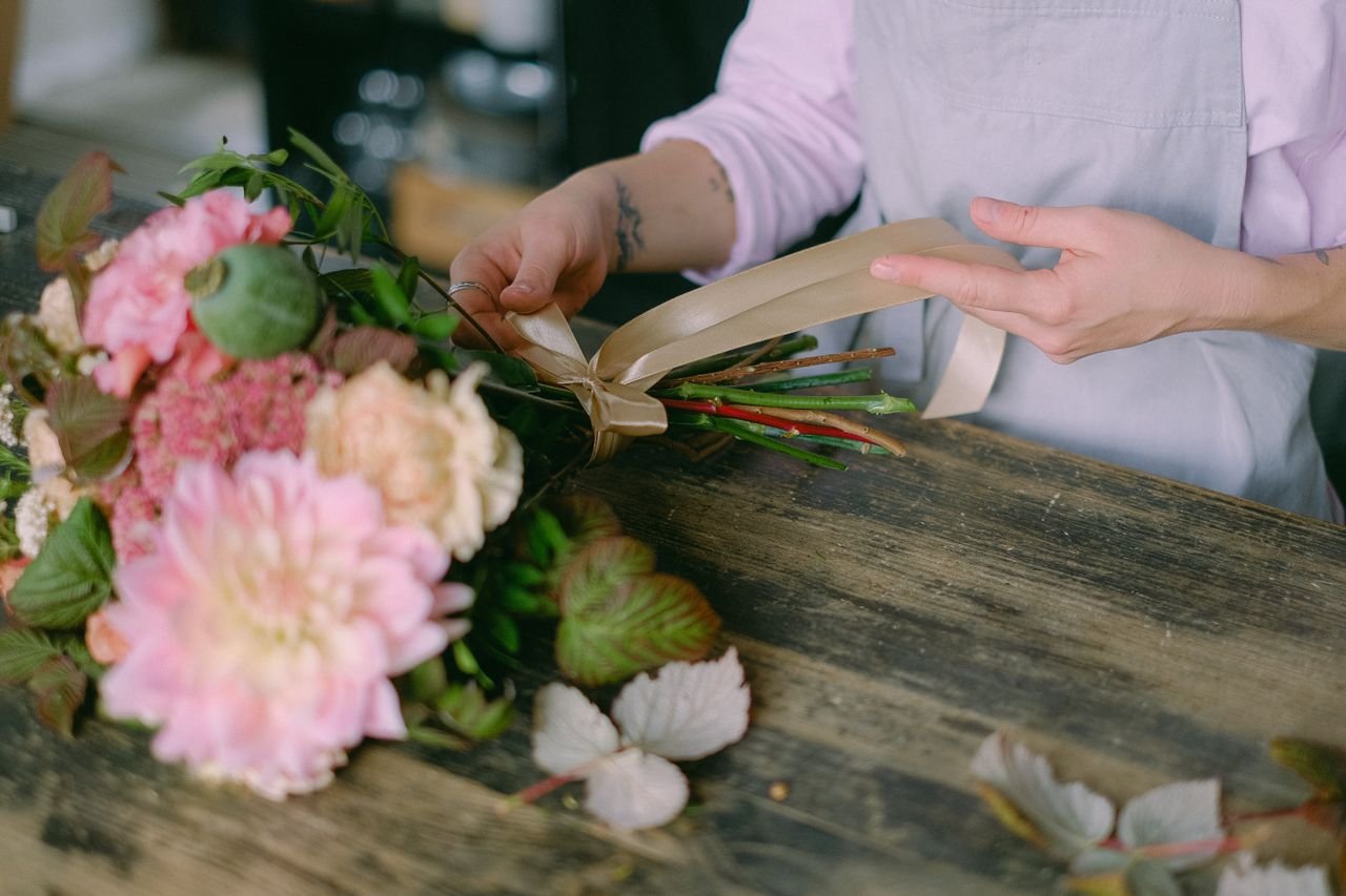 Florist arranging a beautiful floral bouquet with delicate hands and soft petals indoors.